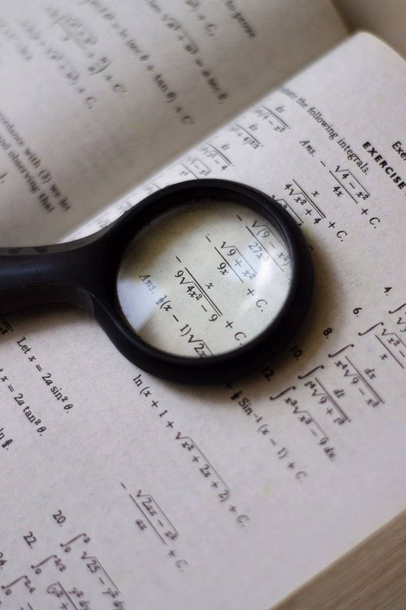 A magnifying glass focuses on mathematical equations in a textbook, highlighting detailed calculations.